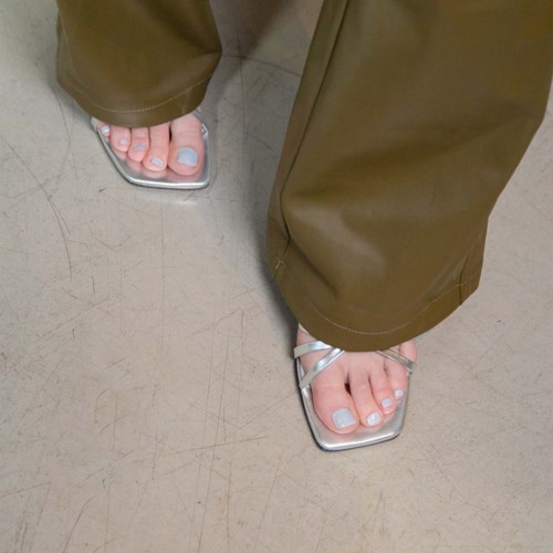 Person wearing brown pants and silver sandals, standing on a gray floor.