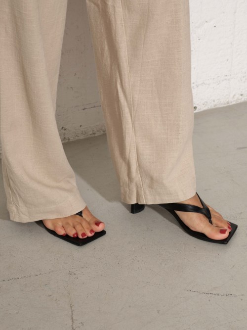Personen har beige byxor och svarta flip-flops. En liten del av deras fötter med röd nagellack syns.