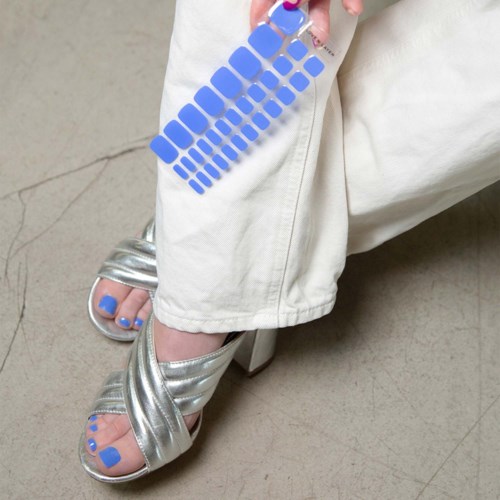 A person wears cream-colored pants, metallic silver sandals, and shows painted toes with blue nail polish.