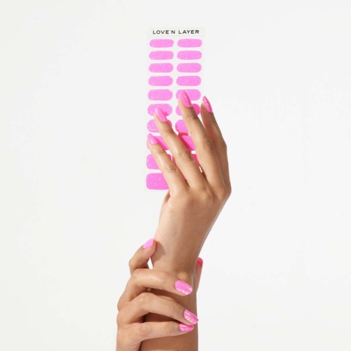 A hand with pink nails points to pink nail polish labels on a white background. The labels say 'Love N Layer'.