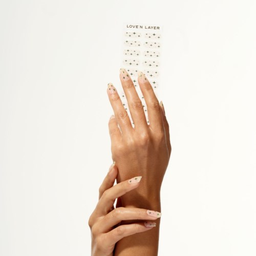A hand with colorful nails touches a sheet of decorative stickers that say "LOVE N LAYER."