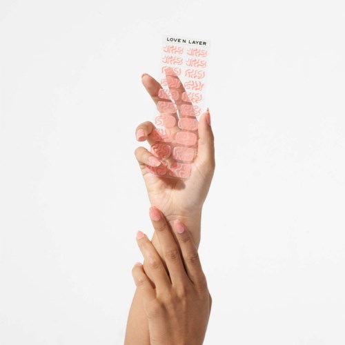 A hand holds a transparent nail sticker with red designs and text in black, reading 'LOVEN LAYER'.