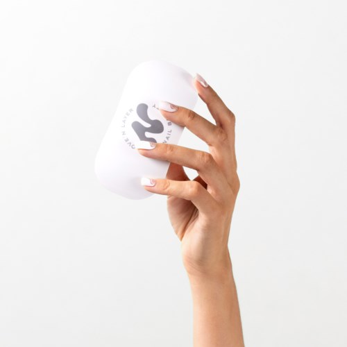 A person holds a white item with black writing, in front of a plain background.