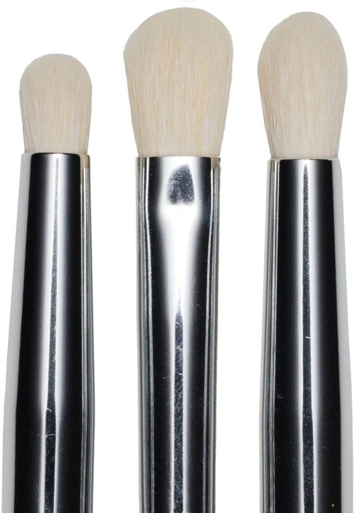 Drie make-up kwasten met houten handvatten en zachte borstels staan naast elkaar.