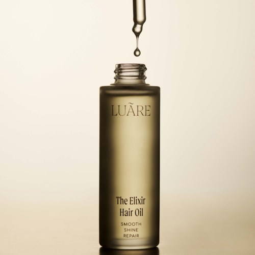 Eine Pipette gibt Öl in eine hohe, goldfarbene Flasche mit der Aufschrift 'LUARE Hair Oil.'