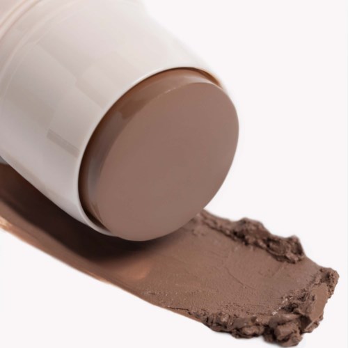 A brown lipstick tube is lying with some lipstick spilled on a white surface.