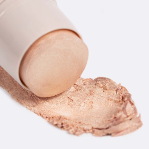 Ein beiger Make-up-Foundation-Tub mit verschüttetem Produkt auf einer weißen Oberfläche.