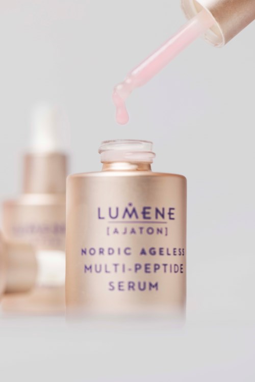 Eine roségoldene Flasche mit Lumene Hautserum mit Tropfer, Nahaufnahme, einfacher Hintergrund.