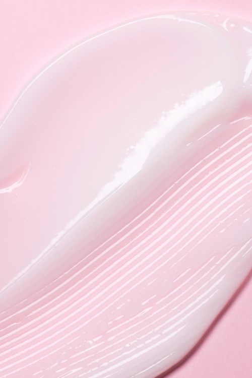 Een gladde, witte crème ligt op een roze achtergrond met strepen en textuur details.