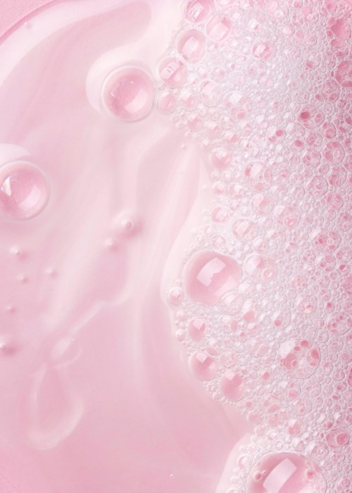 Roze vloeistof met bellen en schuim aan één kant, glad en bruiserig.