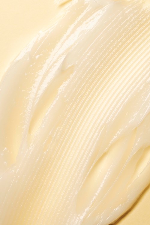 Romige, gladde, gekrulde substantie, waarschijnlijk boter of margarine, met een glanzend oppervlak en lichte gele kleur.