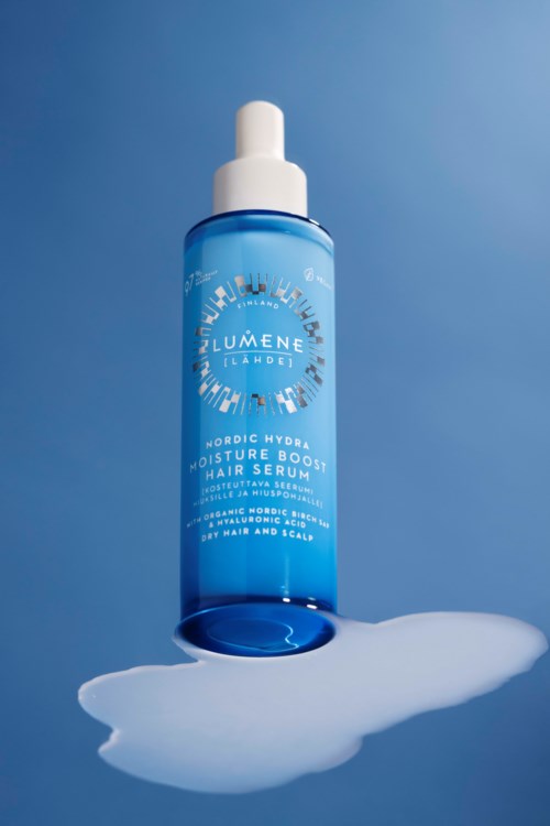Een blauwe fles met haarserum staat op een oppervlak met wat uitgelopen serum eromheen.