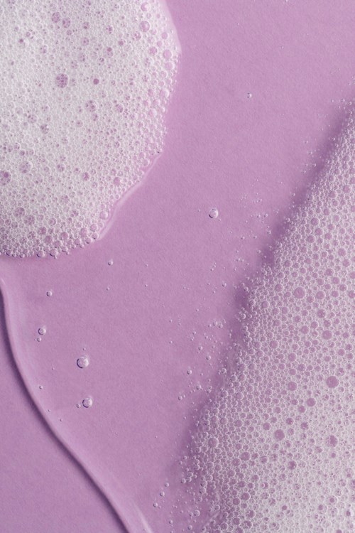 Roze schuim met bellen op paarse achtergrond, glad en schuimig textuur. Het lijkt op zeep- of badschuim.