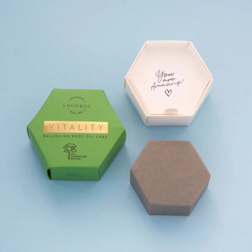 Eine grüne Box mit dem Schriftzug 'Vitality' und eine graue Box liegen auf einer hellblauen Oberfläche. Eine offene weiße Hexagon-Box sagt: 'You are Amazing!'