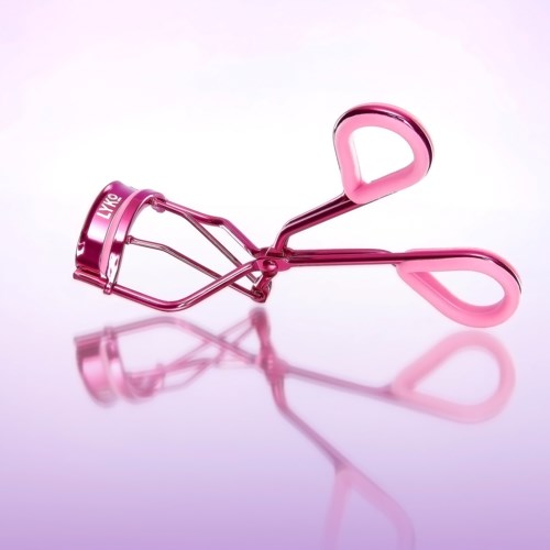 Een roze wimperkrabber met twee handgrepen en een gebogen metalen klem op een reflecterend oppervlak.
