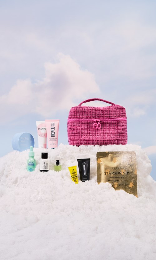 Pink bag, few skincare products, and a gold-colored item on snow under cloudy sky.
