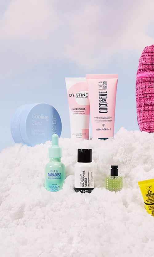 Various skincare products placed on snow, including creams, serums, and a small yellow item, with a pink woven item nearby.