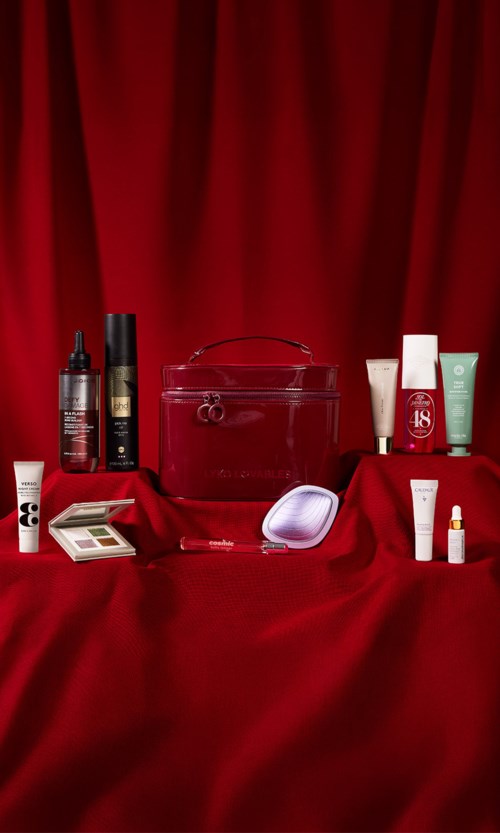 Verschiedene Hautpflege- und Make-up-Produkte auf roter Fläche mit rotem Vorhang im Hintergrund.