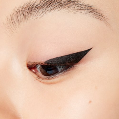 A close-up of a person's eye with black eyeliner and sparse eyebrows.