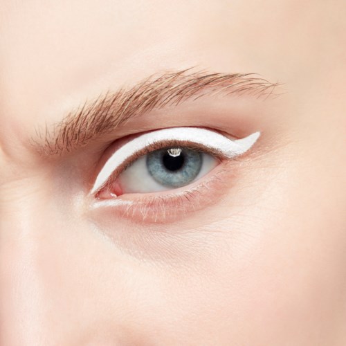 Close-up of a blue eye with white eyeliner on the upper eyelid and natural skin.