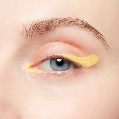 Ett öga med gul ögonmask på ögonlocket, klar hud och blonda ögonbryn.