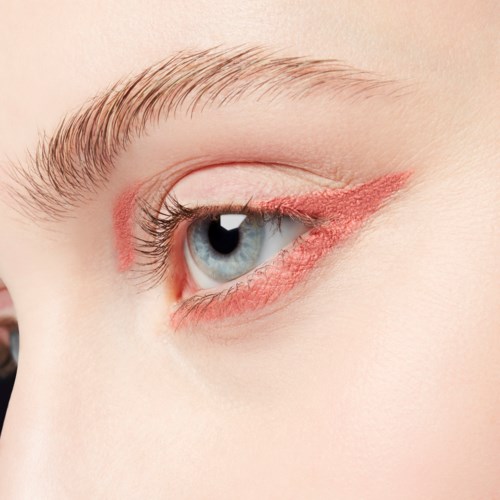 Närbild av ett blått öga med smink, visar ögonfransar, ögonlock och röd eyeliner.