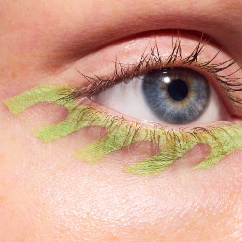 Close-up of a blue eye with yellow-green eye shadow under the eye and on eyelids.