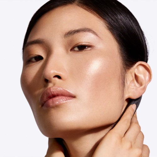A woman with smooth skin, black hair, and a serious expression touches her neck.