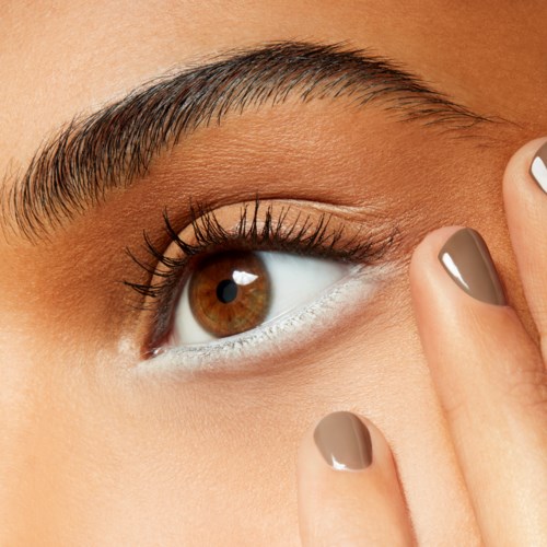 Close-up of a person's eye with well-groomed eyebrows and neatly painted nails. The person is touching their eyelid.