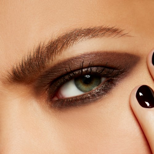 A close-up of a woman's eye with makeup, eyebrow, and her fingers with black nail polish.