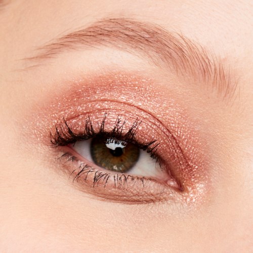 Ett nära foto av ett öga med ljus makeup, inklusive glitterögonskugga och långa fransar.
