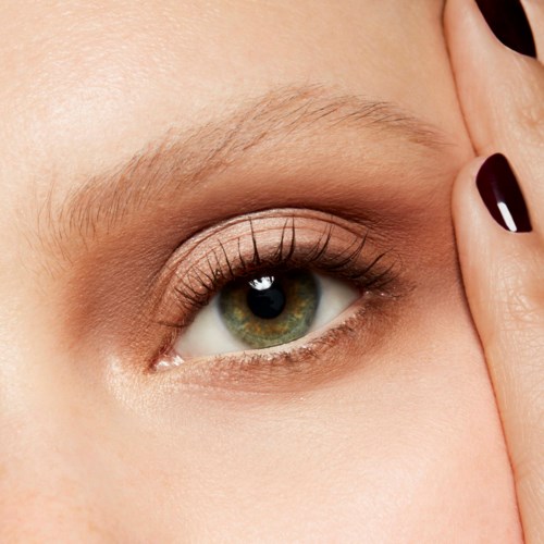 Närbild av ett mänskligt öga med makeup, långa ögonfransar och välskött ögonbryn. Någons hand nära ansiktet.