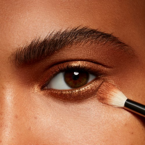A person is applying makeup under their eye with a small brush.