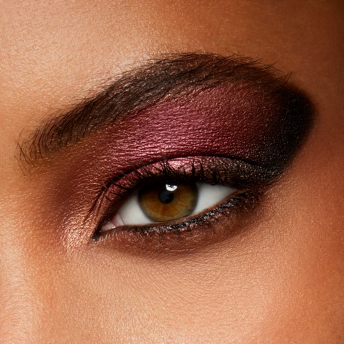 Close-up of a person's eye with dark and purple eye makeup, long eyelashes, and neatly shaped eyebrow.