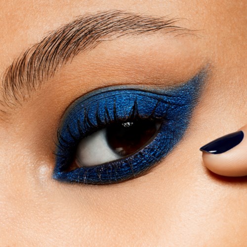 Close-up of an eye with bold blue eyeshadow and long lashes, skin smooth and eyebrow well-groomed.