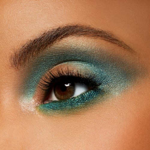 Close-up of a person's eye with green and blue eye makeup and well-groomed eyebrow.