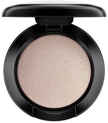 A round, black compact containing a shiny, beige eyeshadow or makeup product with a slight shimmer.
