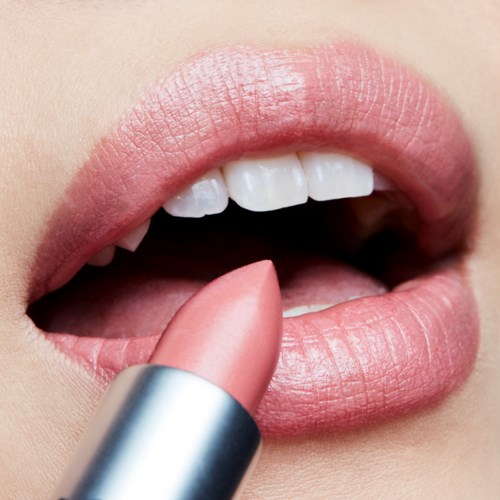 Close-up van lippen met lippenstift dat wordt aangebracht, toont gladde, roze lippen en witte tanden.