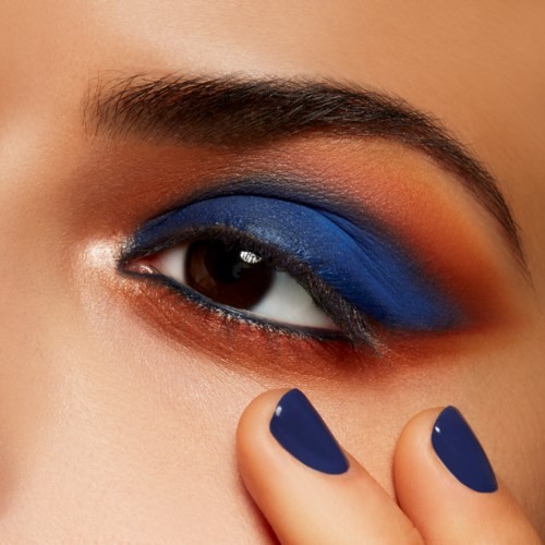 Närbild av en persons öga med blå och orange ögonskugga och matchande blå nagellack.