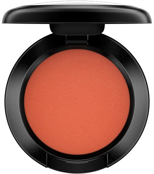 A compact makeup blush with a peachy-orange color in a black case with a lid.