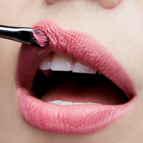 Närbild av läppar med lite rosa läppstift som appliceras med en pensel.