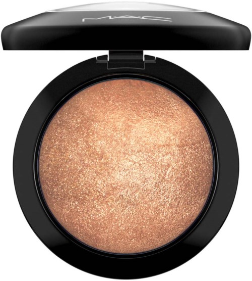 A round, black cosmetic compact with a shiny, beige, shimmering powder inside. MAC logo on the lid.