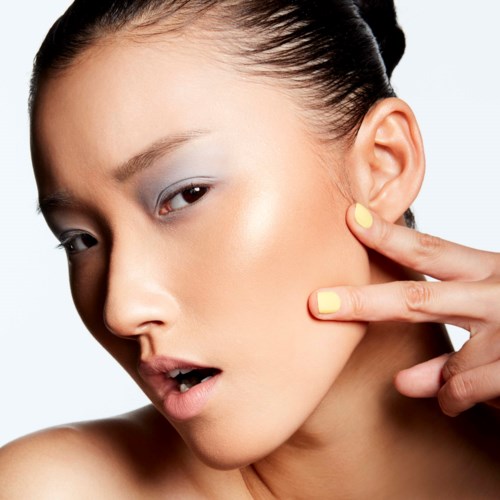 A woman with styled dark hair, makeup, and painted nails touches her cheek with fingers near her face.
