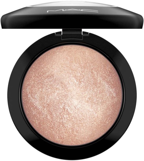 A compact with shiny peach-colored powder inside and a black lid that has the brand name MAC on it.