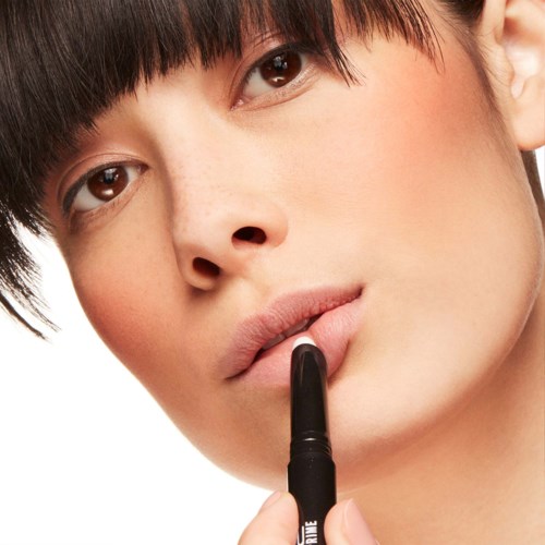 A young person with short dark hair is holding a black lipstick or marker near their lips.