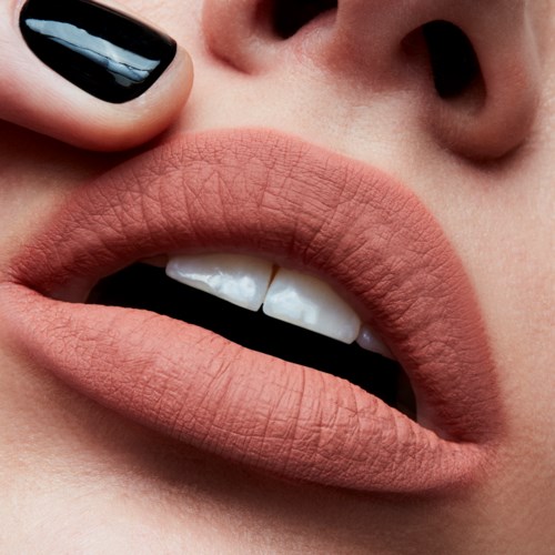 Close-up of lips slightly parted, with a finger touching the upper lip. The lips are smooth and nude-colored.