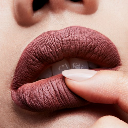 Close-up of lips with lipstick, finger touching lips, and nose visible in the background.