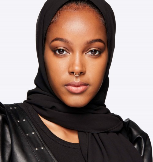 En kvinna med svart headscarf och skinnjacka tittar självsäkert mot kameran.