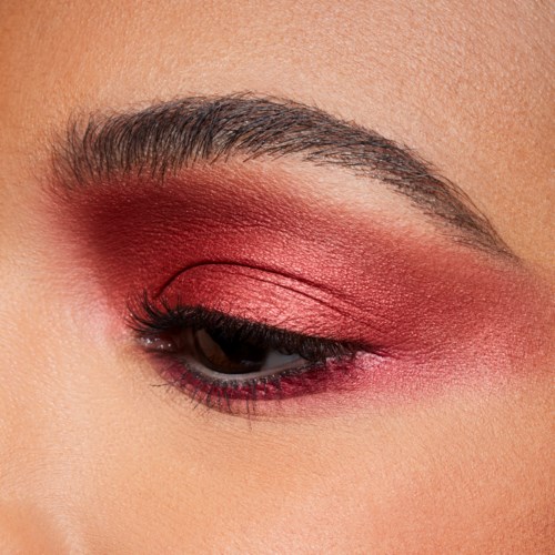 Close-up of an eye with pink and red eyeshadow, and long eyelashes. Eyebrow is well-groomed.
