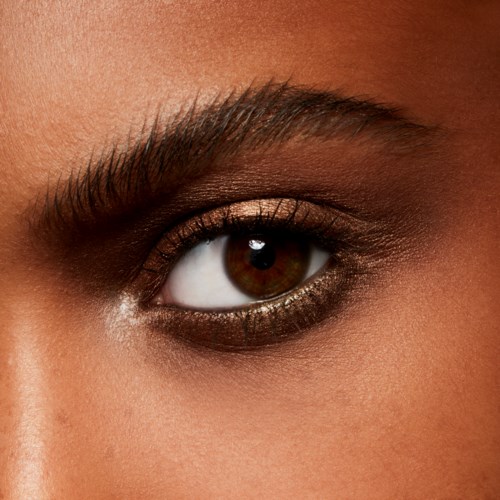 Close-up of a person's eye with eyebrow, brown iris, and makeup. Skin is smooth and well-groomed.